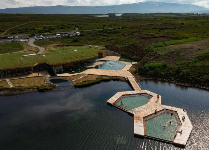 Several pool basins and accompanying wooden walkways float on a lake with mountains in the background.