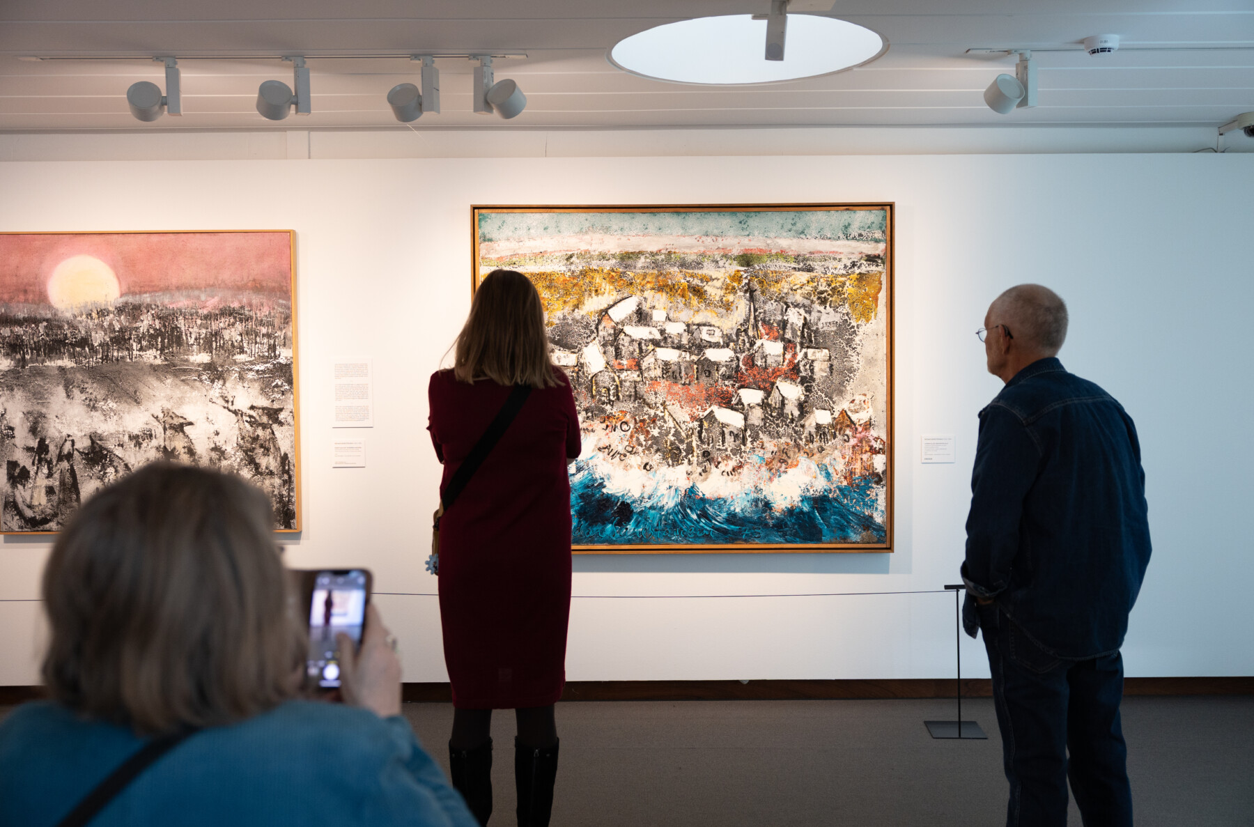 Several people are looking at paintings in a gallery.