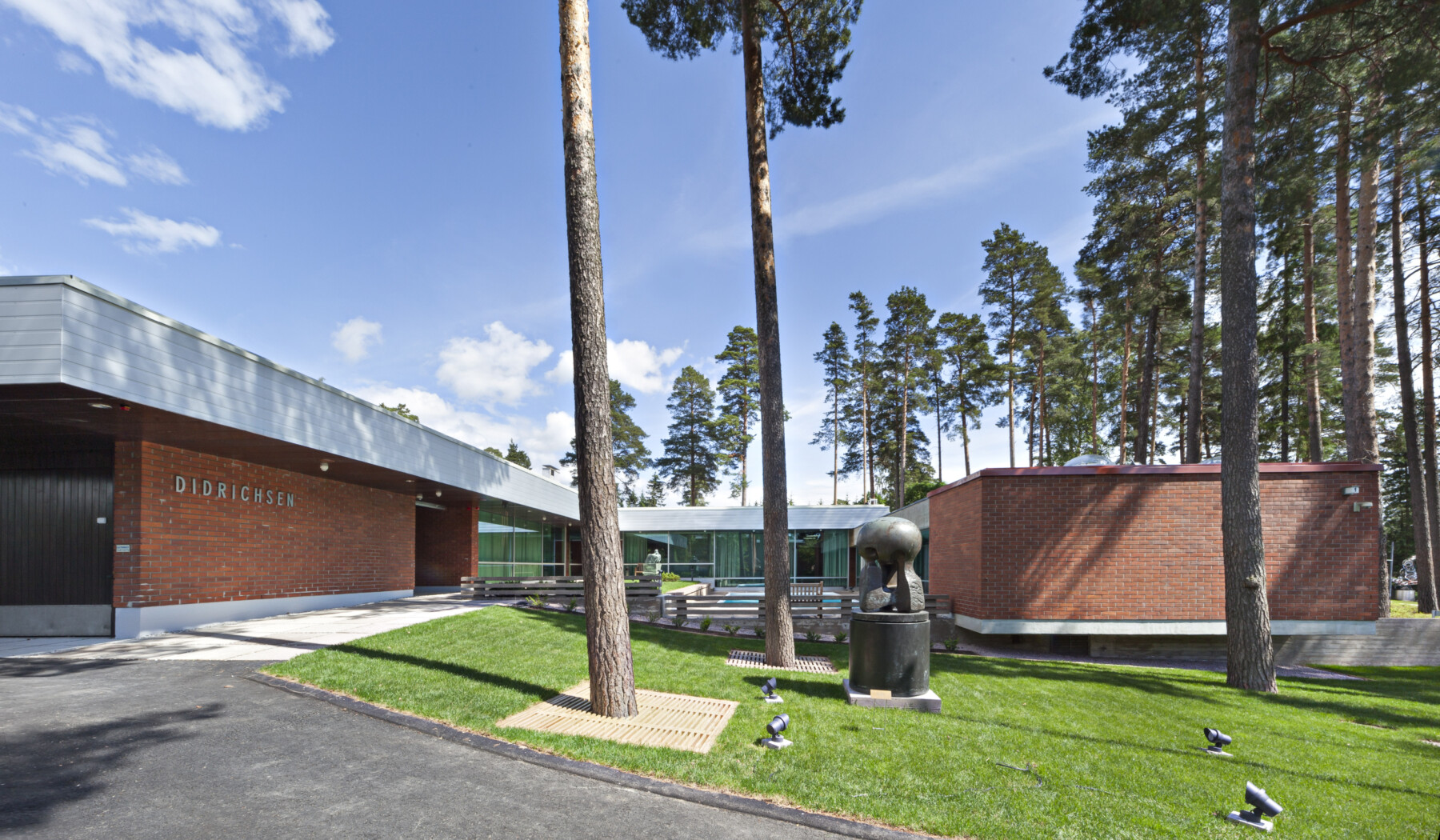 Trees and sculptures decorate the yard in front of a one-story brick building.