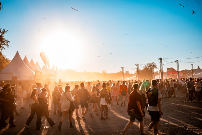 A large crowd in a festival area as the sun shines.