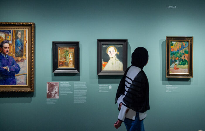 A person walks past several paintings hanging on a gallery wall.