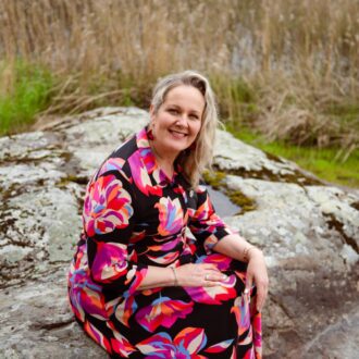 A smiling woman sitting on a rock by a lake.