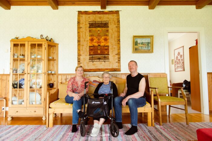 Three people sitting on a sofa in a traditionally furnished living room.