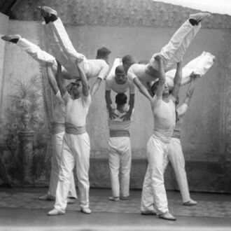 A group of Finnish high school boys in white uniforms poses with several of them lifting several others into the air.
