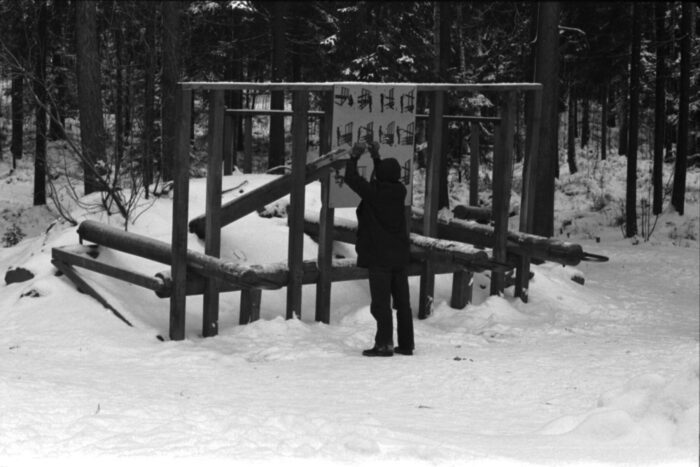 A man exercises on wooden outdoor fitness equipment located in a wintery forest.