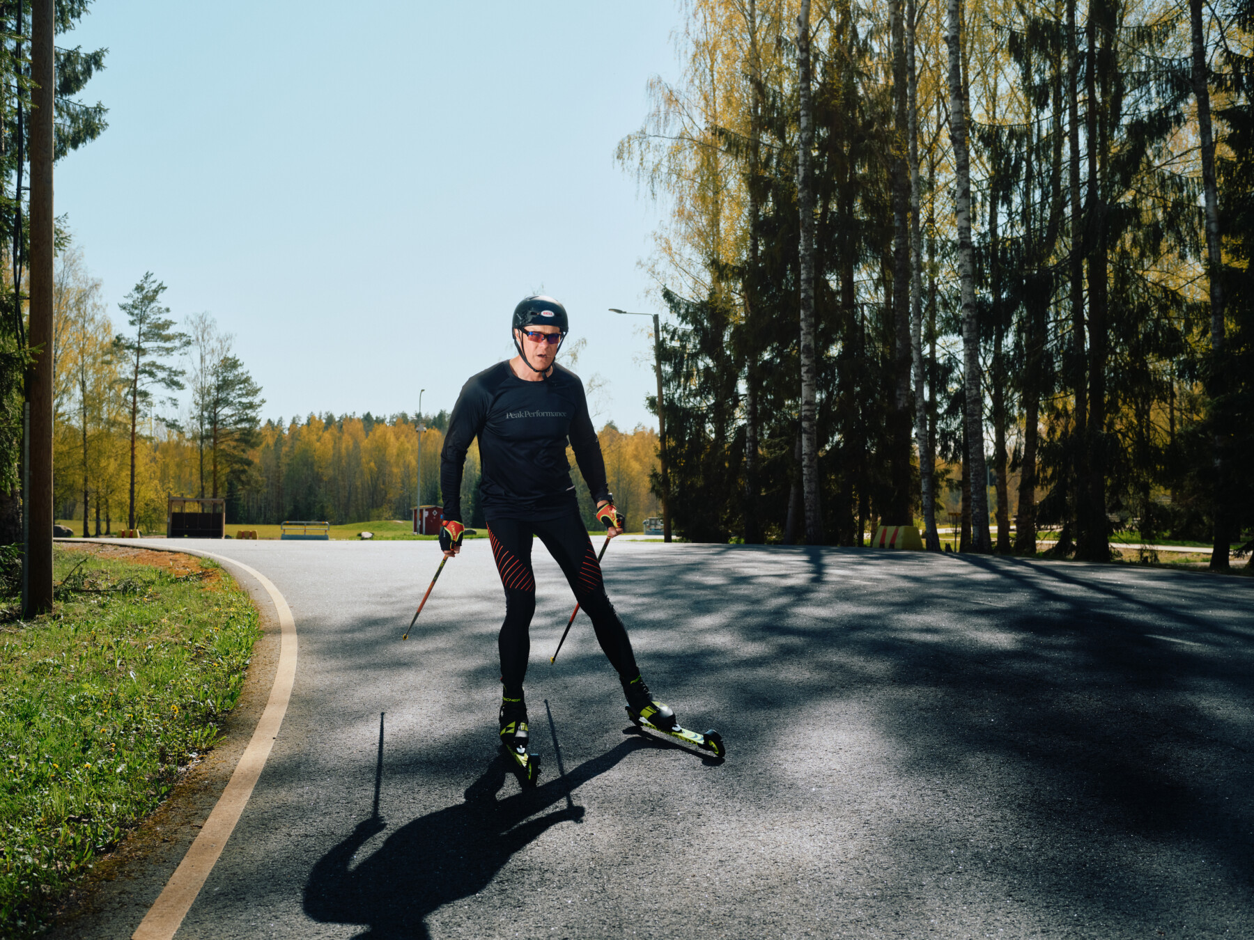 A man roller-skis on an asphalt path lined with trees.
