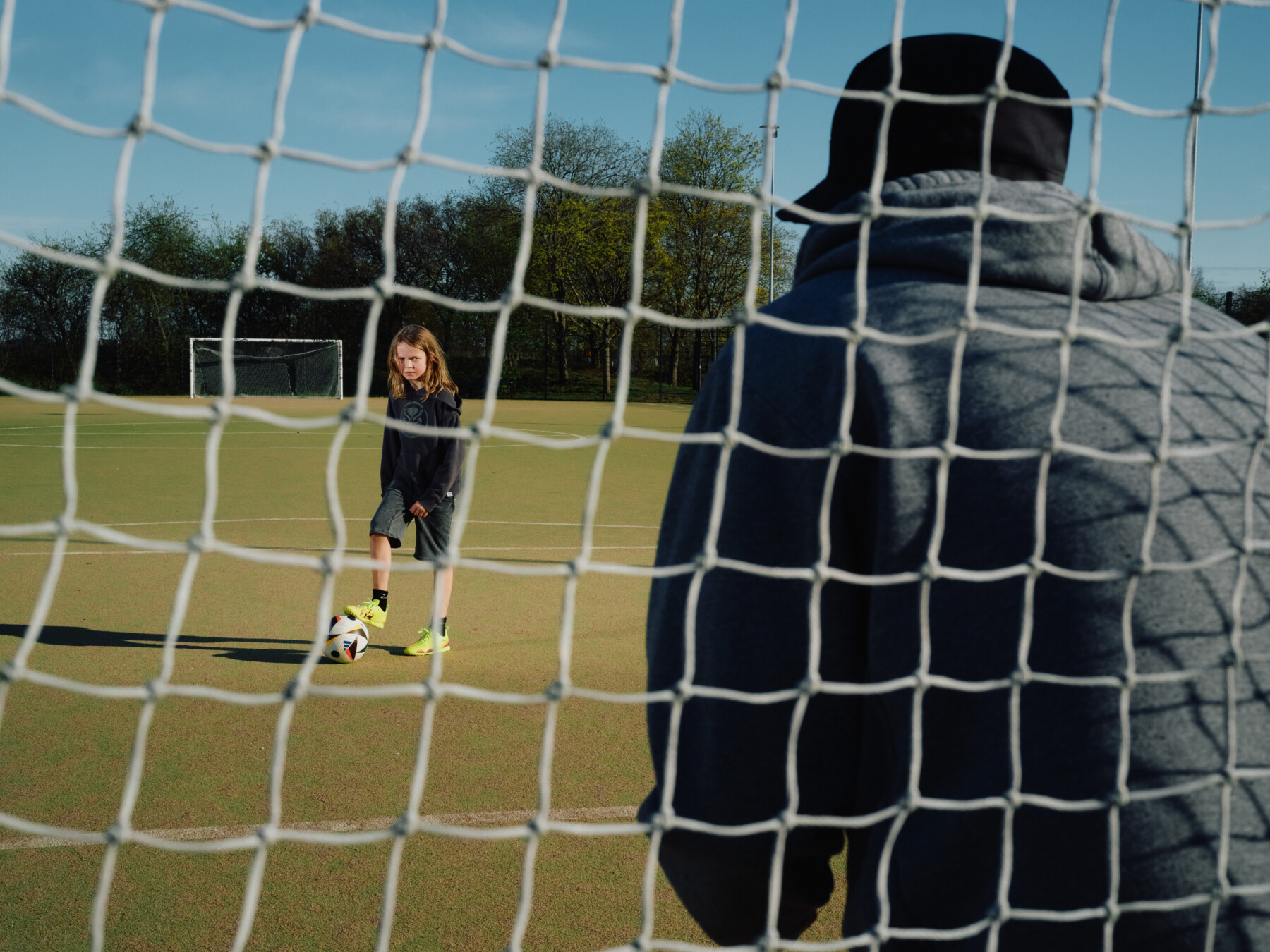 A boy kicks a football toward a goal.