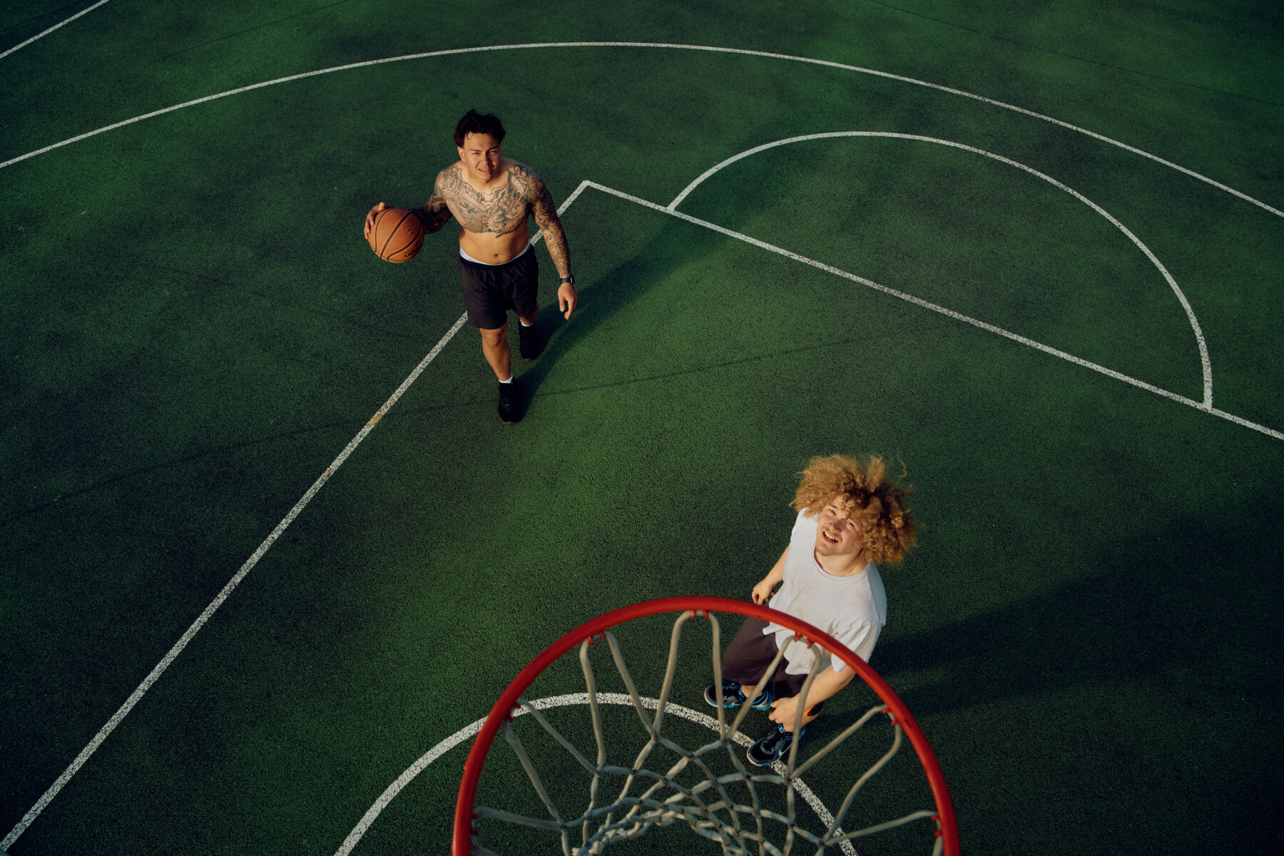 Two young men play basketball outdoors.