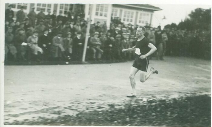 A Finnish athlete runs in front of a crowd of spectators in the 1920s.