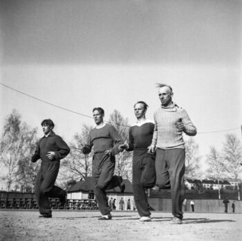 Four men run on a sports field in a historical black-and-white photo.