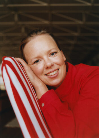A woman smiles while reclining against a red-and-white-striped chair.