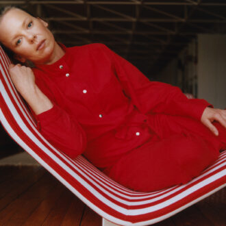 A woman reclines on a red-and-white-striped chair, gazing thoughtfully into the camera.