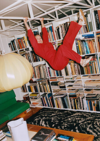 A woman playfully swings her feet while holding on to a metal bar in the ceiling structure of a home library.