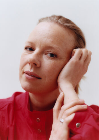 A woman rests her head on her hand and looks calmly and confidently into the camera.