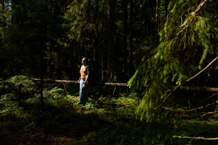 Sunbeams fall on a woman looking up at the sky in a dim spruce forest.
