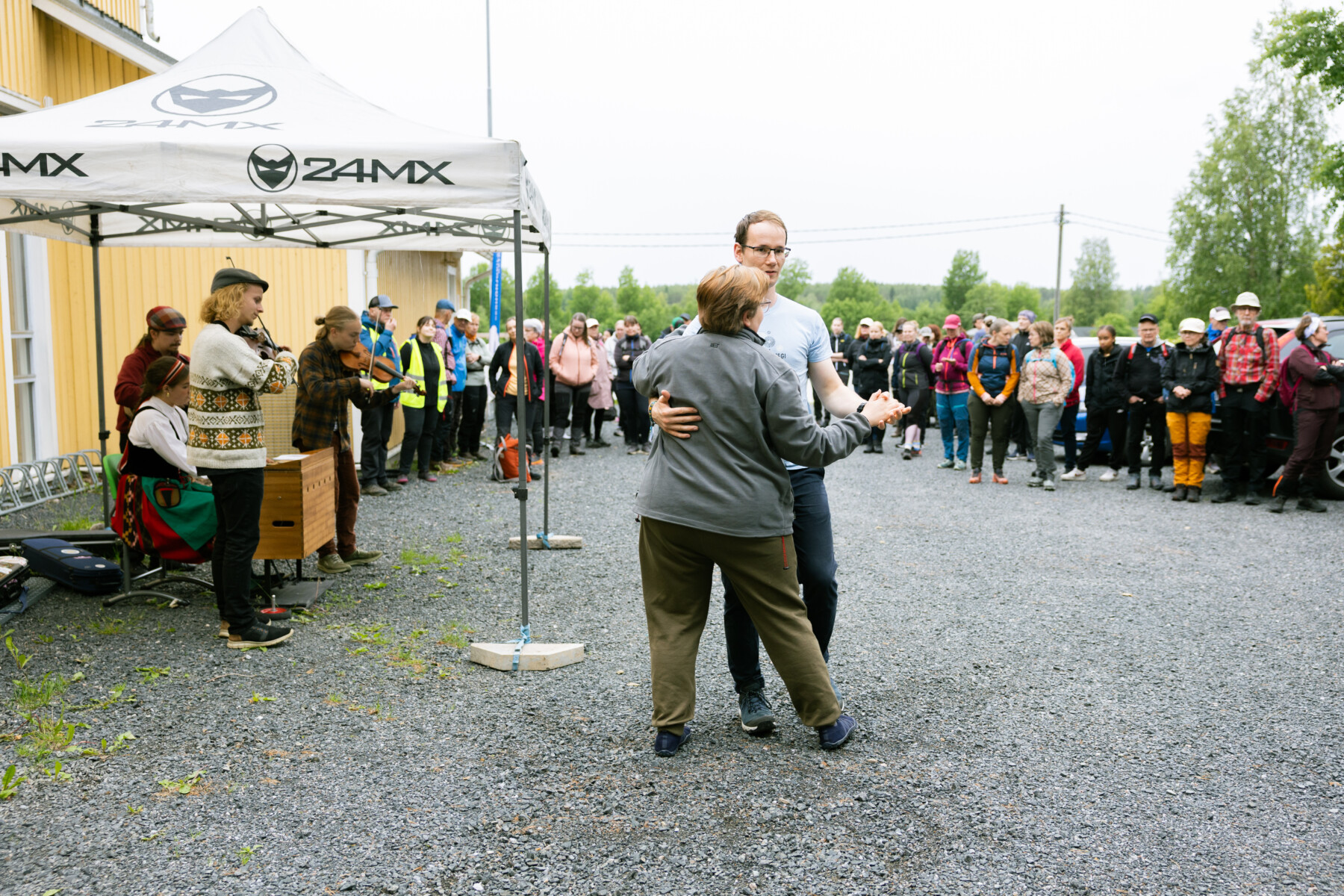 Two people dance in front of musicians as a crowd of people watch.