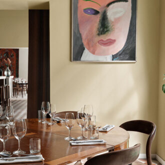 A round wooden dining table sits ready beside a window in a cozy restaurant.