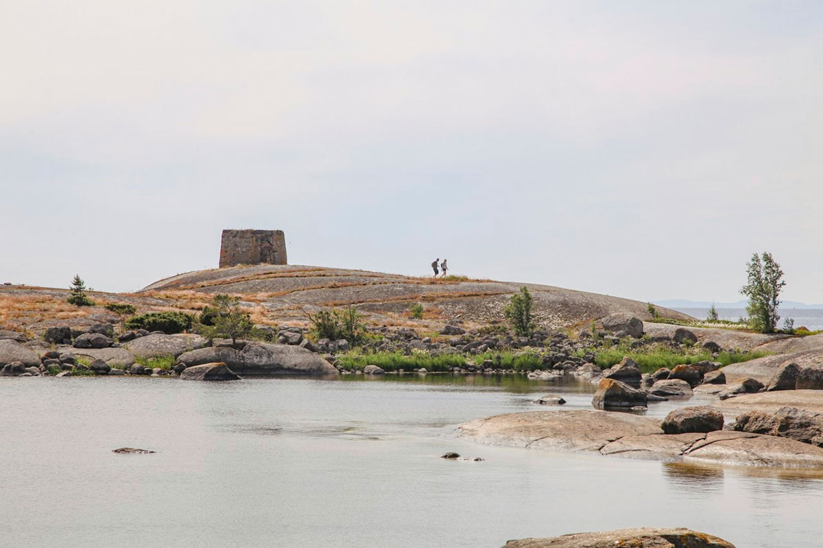 Two people walk across a rocky island landscape with sparse vegetation.