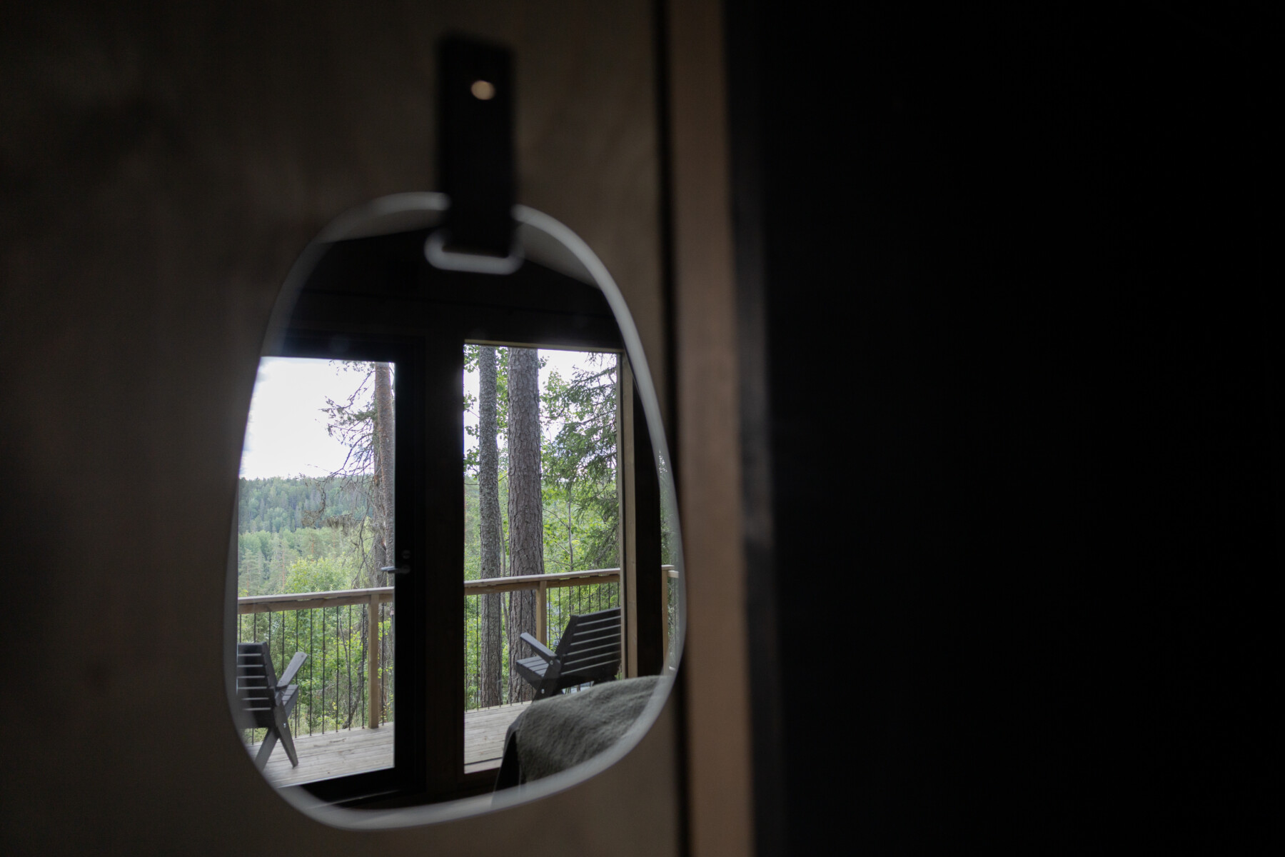 A round window reveals two reclining chairs on a balcony overlooking a dense green forest.