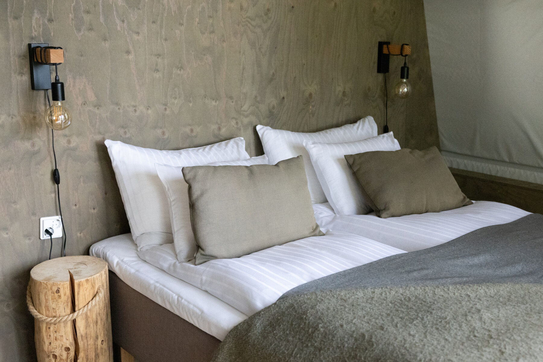 A neatly made double bed with minimalist decor stands inside a softly lit room.