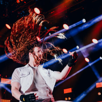A man in fingerless gloves plays an imaginary guitar, whipping his long hair.