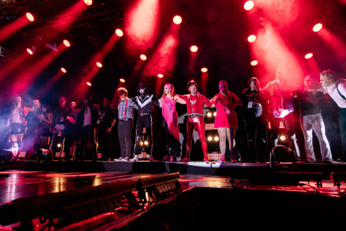 Many people stand in line on a stage. Some are wearing colourful costumes.