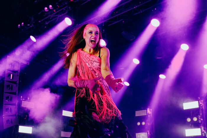 A woman in a dress and thick gloves sings as she plays an imaginary guitar.