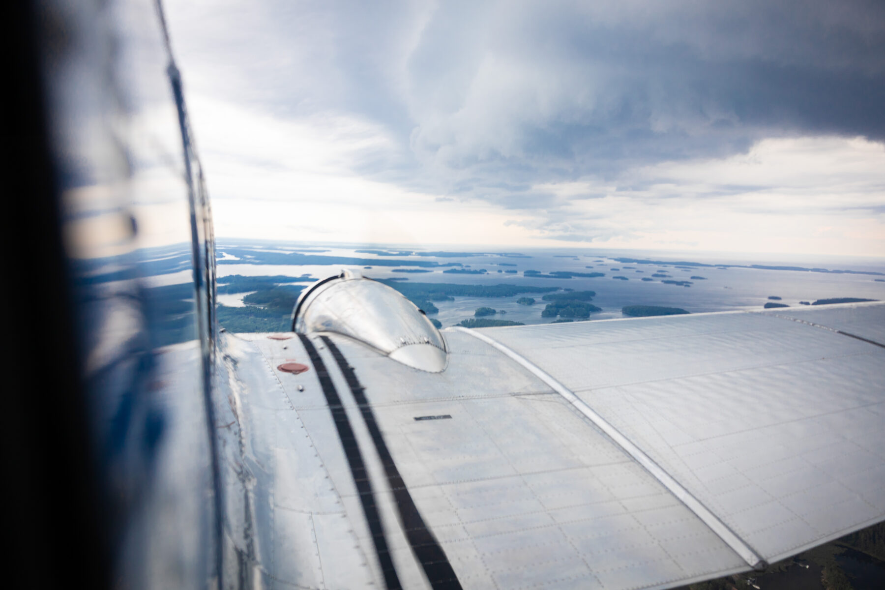 Através da janela de um avião, uma asa se estende sobre a água e as ilhas sob um céu nublado.