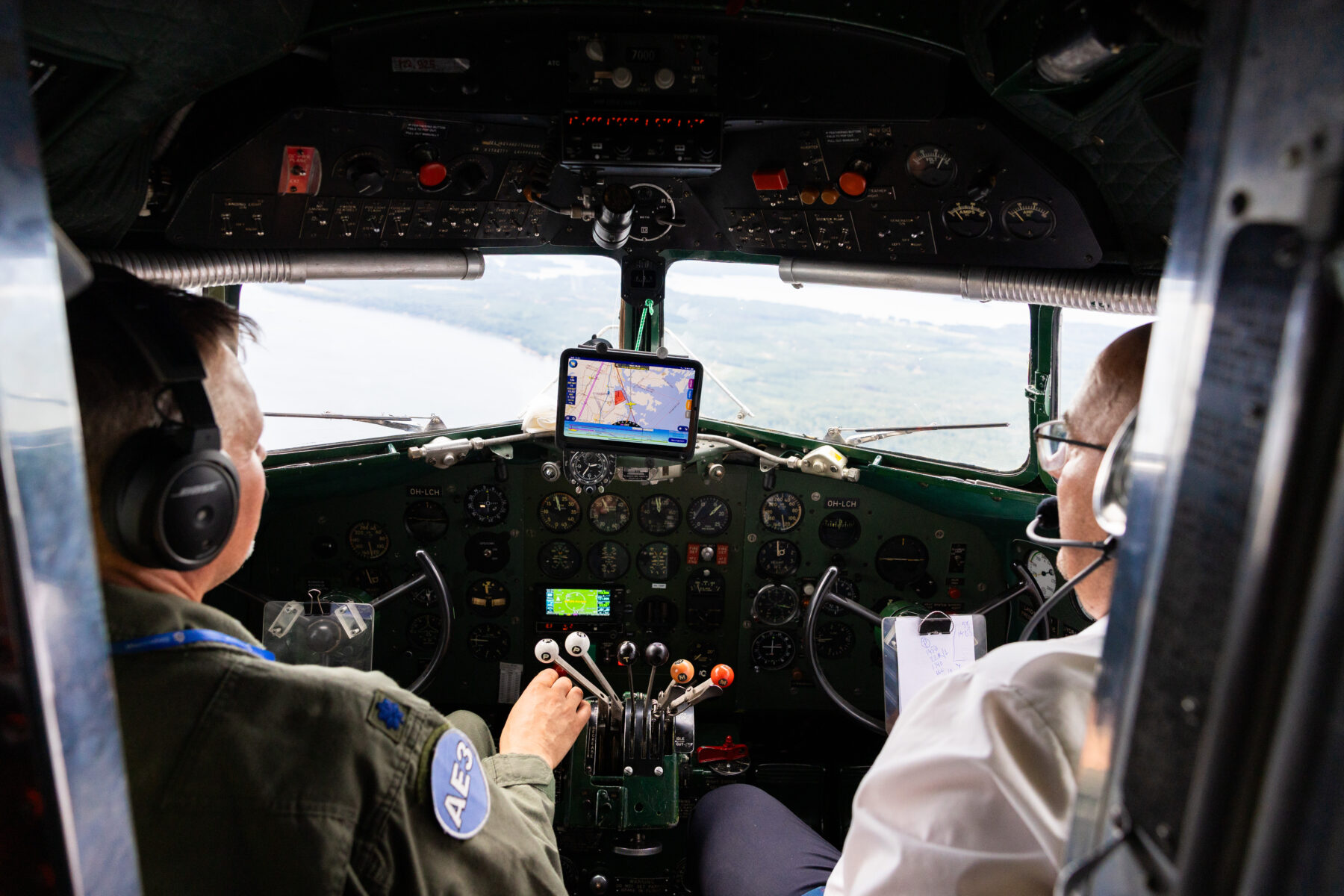 Dois pilotos na cabine de um avião antigo navegam usando um tablet eletrônico montado no painel.