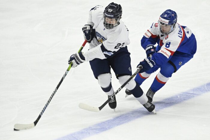 Two ice hockey players chasing the puck in an ice rink.