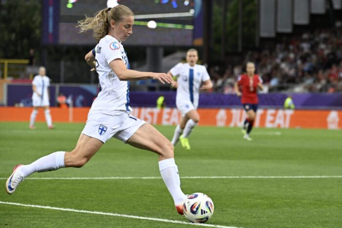A female footballer kicking a ball in a football stadium.