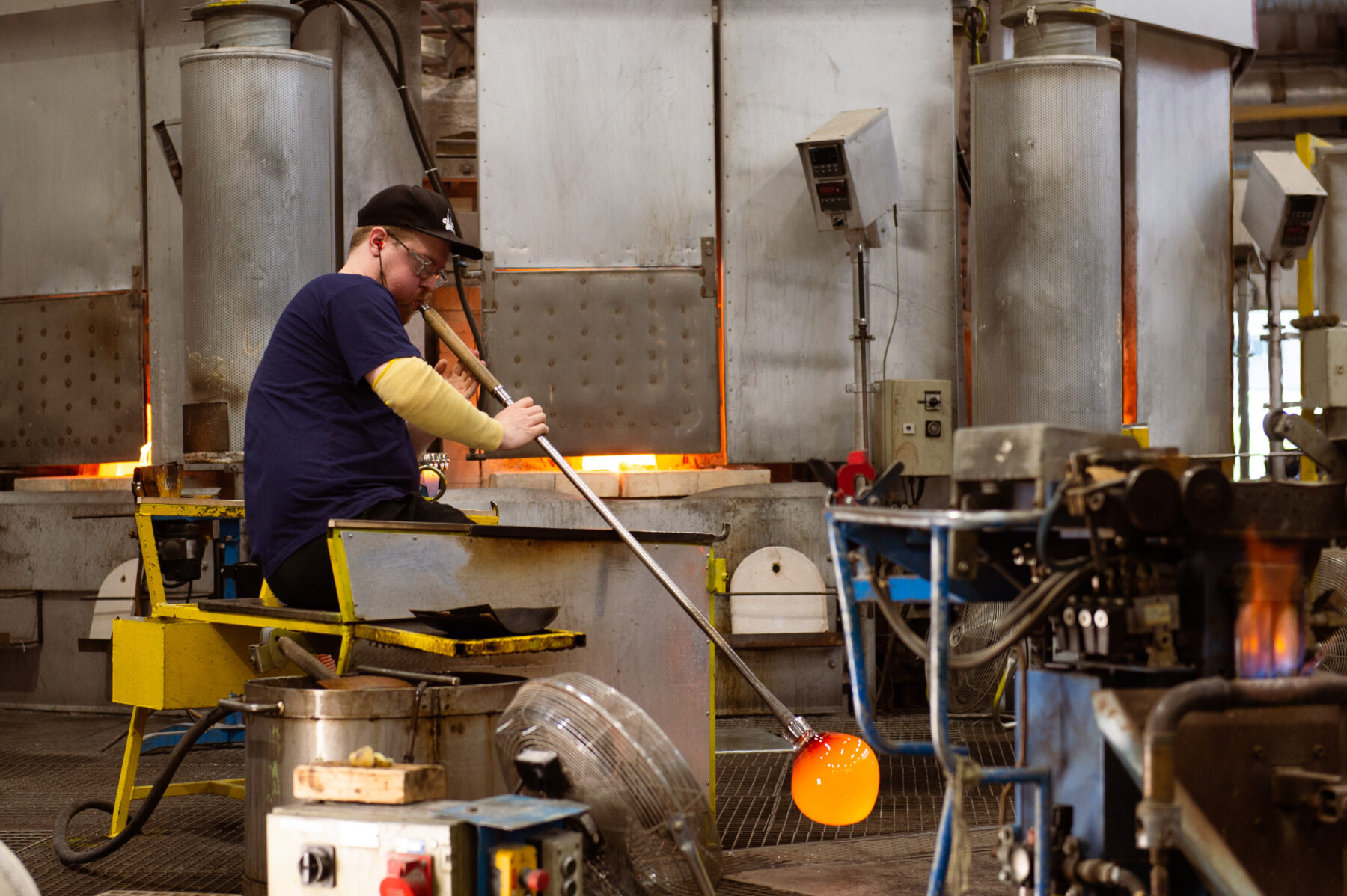 Un homme utilise une longue tige métallique pour manipuler du verre en fusion dans un atelier.