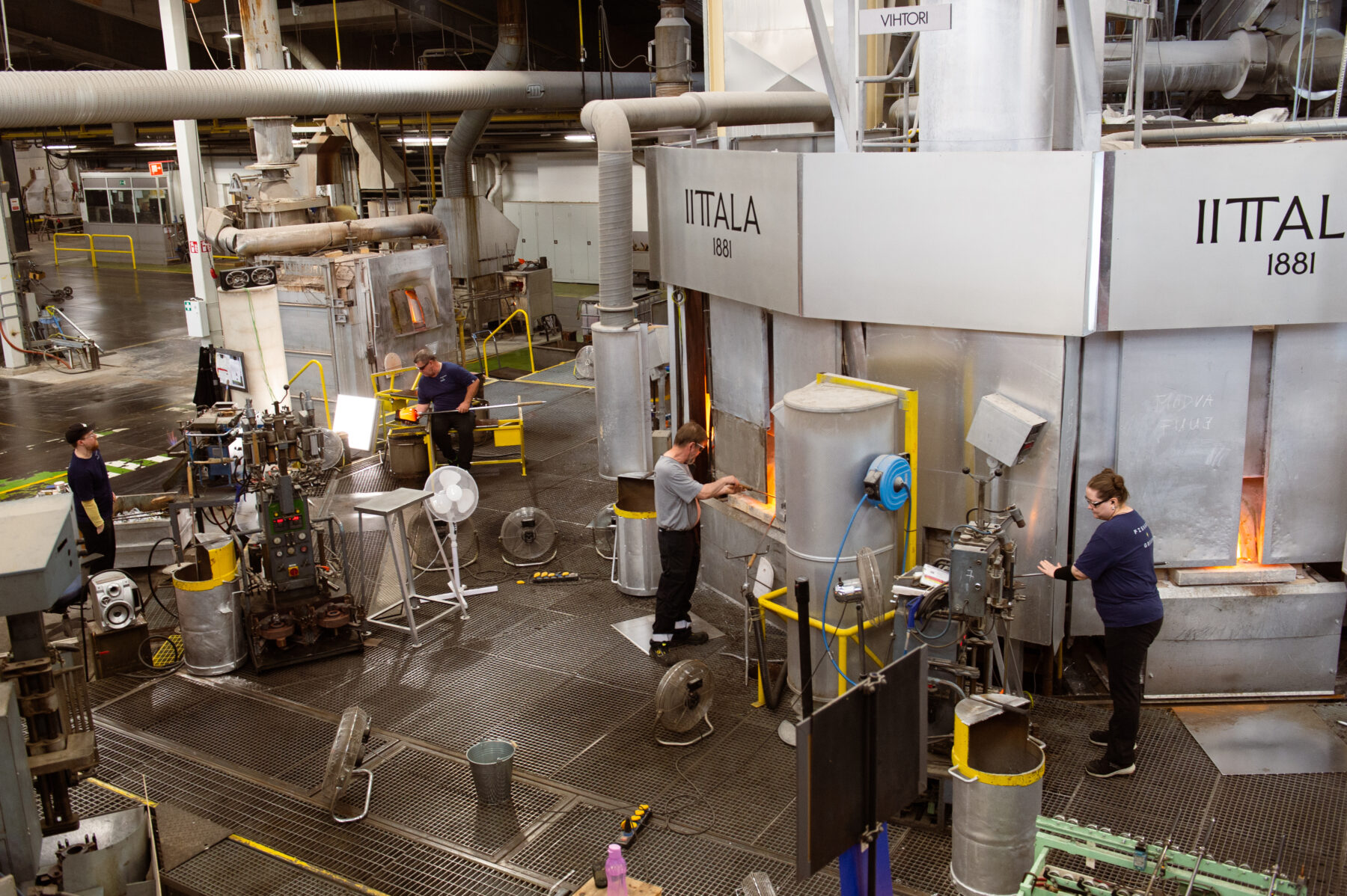 Dans un environnement industriel, plusieurs ouvriers participent aux différentes étapes du processus de production du verre à proximité de différents équipements industriels de taille imposante.