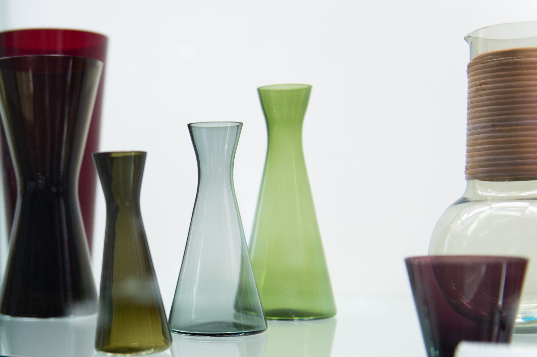 Un certain nombre de vases en verre de différentes couleurs, formes et tailles sont présentés sur une surface blanche réfléchissante.