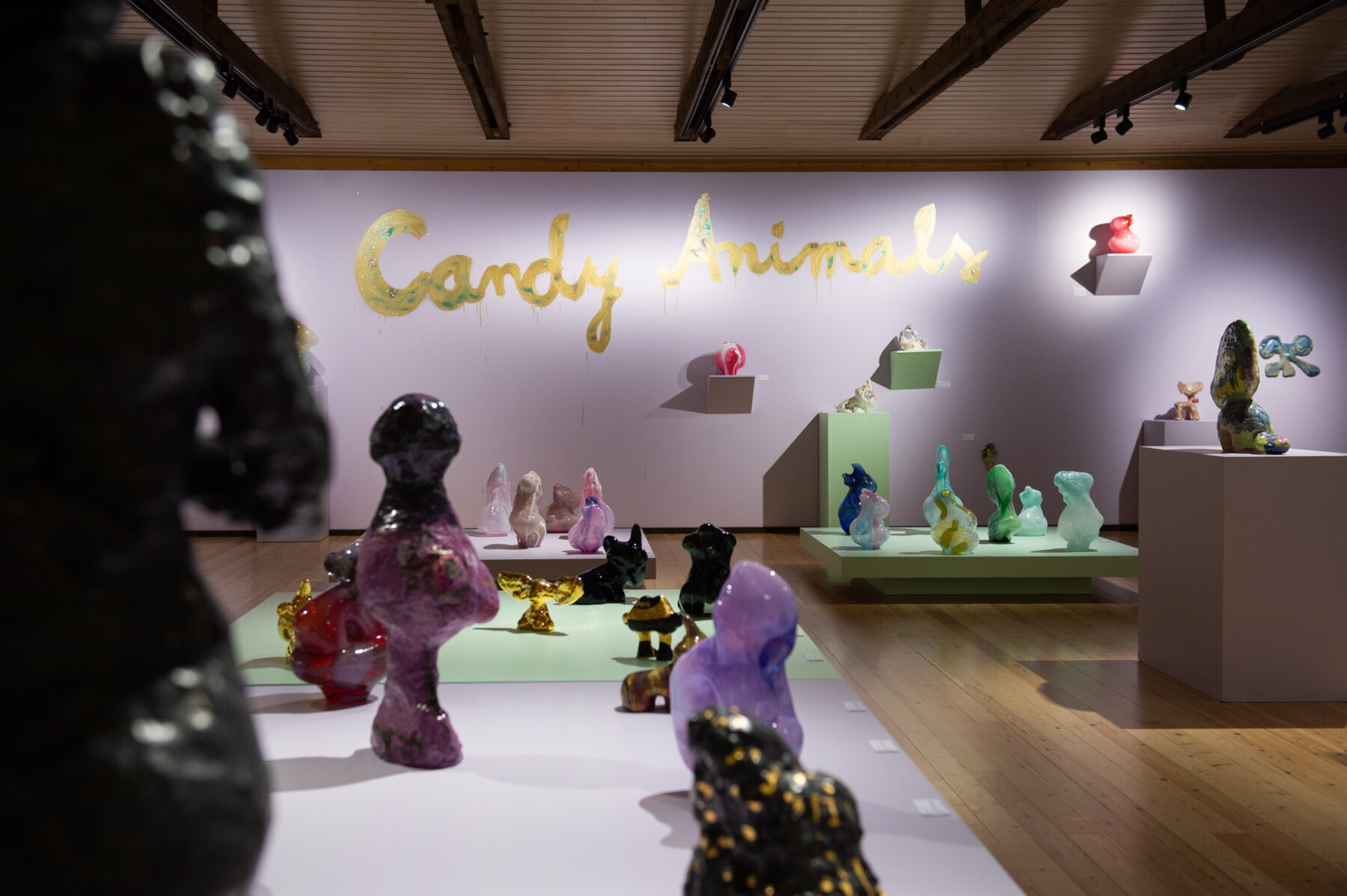 Des sculptures animalières en verre et en céramique de différentes tailles sont exposées dans une salle de musée, avec le titre de l’expo « Candy Animals » inscrit sur le mur en fond de salle en lettres cursives dorées.