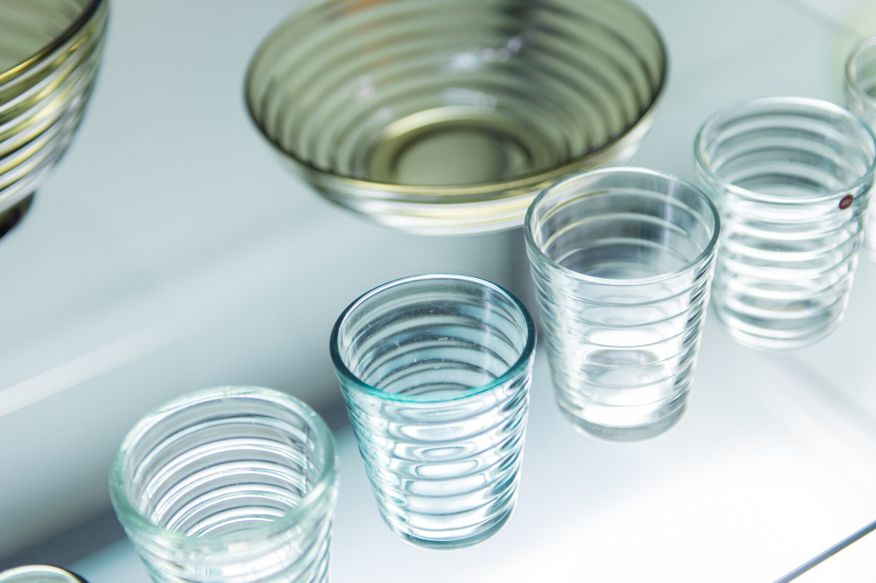 Des saladiers en verre transparent et des verres aux motifs concentriques striés sont disposés sur une surface blanche.