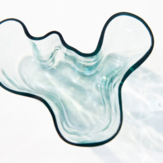 Un vase ouvragé en verre bleu clair repose sur une surface blanche.