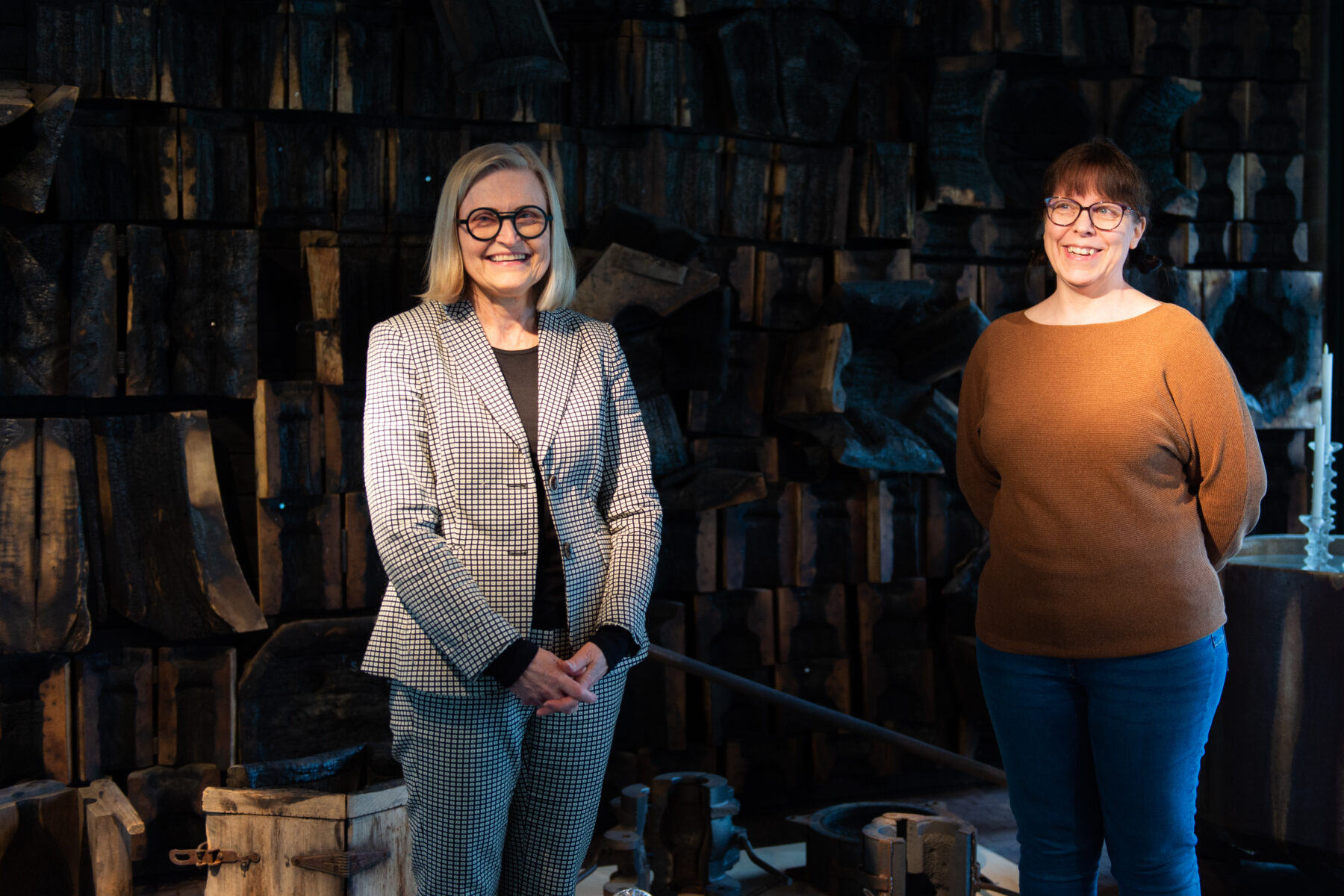 Deux femmes tout sourire se tiennent côte à côte devant des étagères remplies de divers objets anciens patinés par le temps.