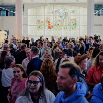 A crowd of people is talking and laughing at a party in a large airy hall.