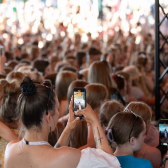 At an outdoor music performance, a crowd of people is watching, some of them taking pictures with their phones.