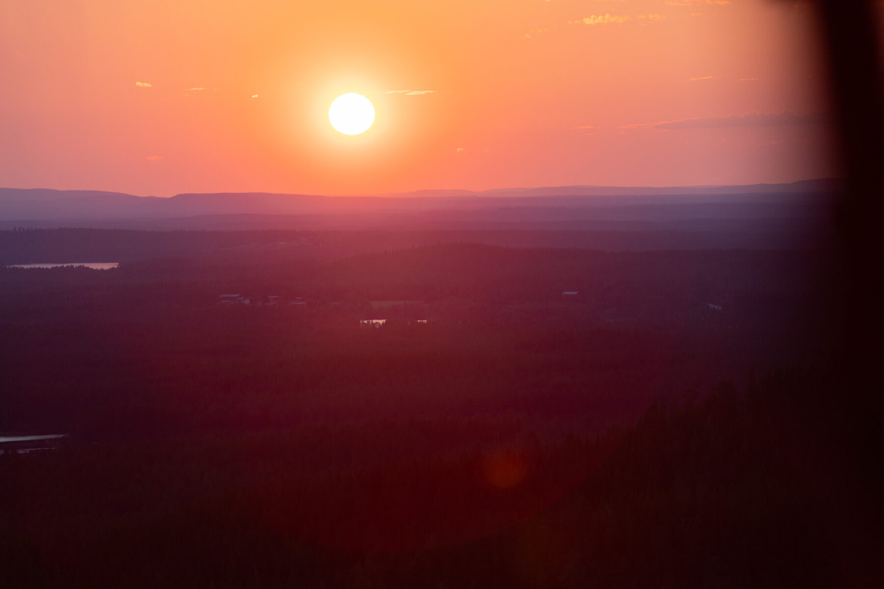 A sunset casts a warm glow over a landscape of dark forests and distant mountains.