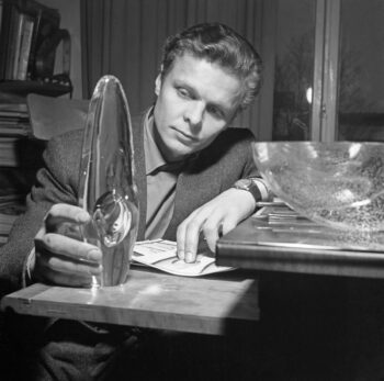 Un homme assis à un bureau examine un objet en verre transparent en forme de larme.