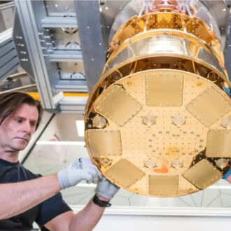 Two technicians wearing gloves work on a cylindrical, metallic piece of machinery.