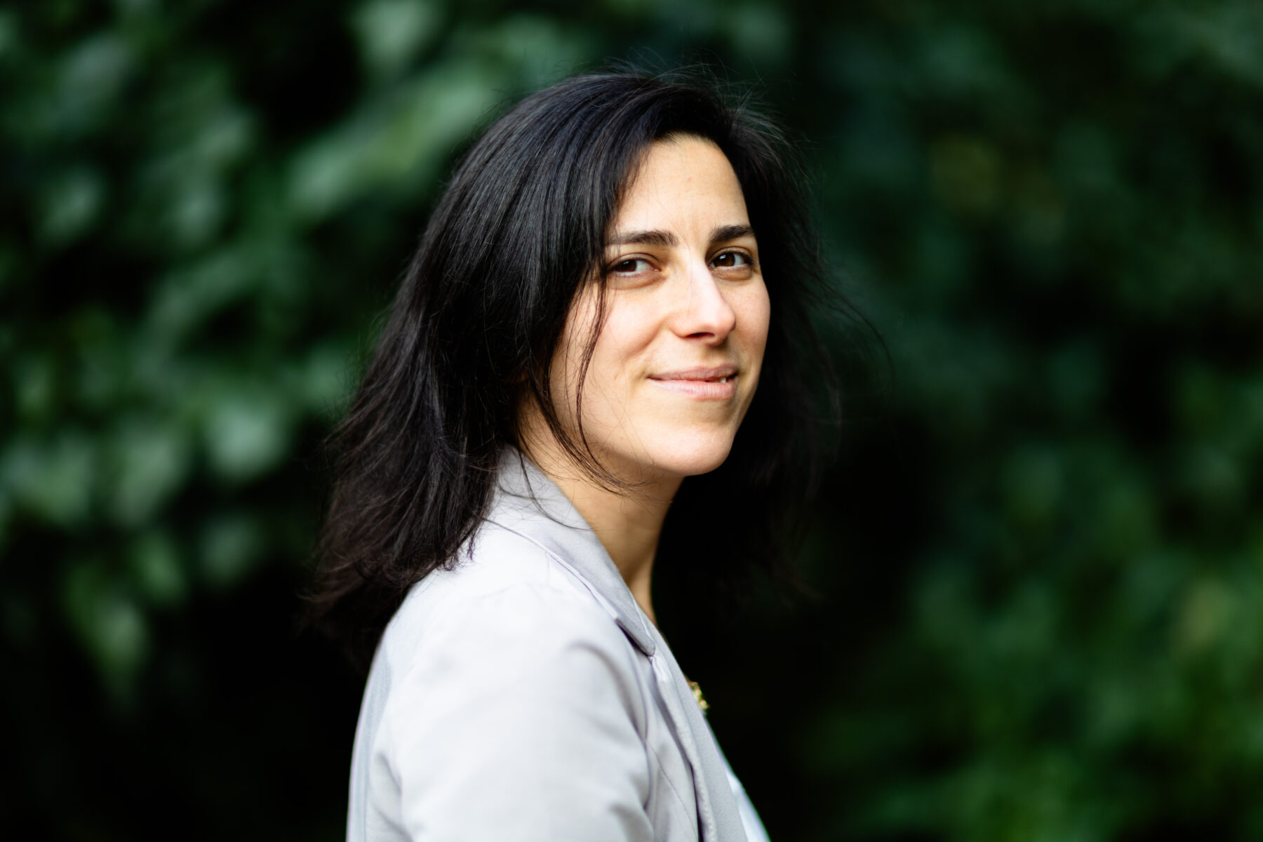 Uma mulher em frente a uma densa folhagem verde, sorrindo para a câmera.