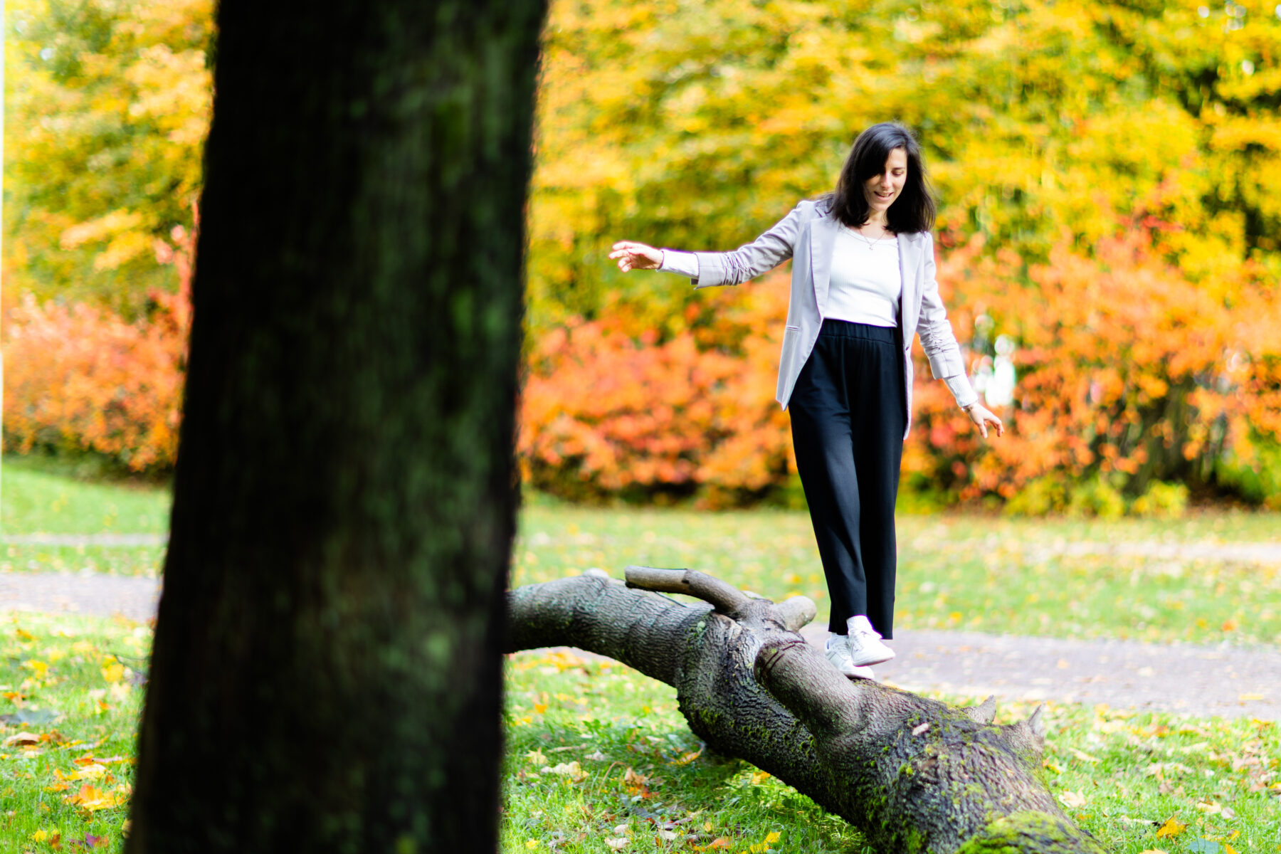 Uma mulher caminhando sobre um tronco de árvore caído em um parque no outono.