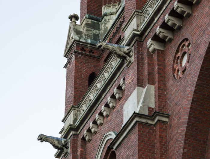 A grand, red-brick church with two pointy towers features gargoyles that stick out from the building’s edges and corners.