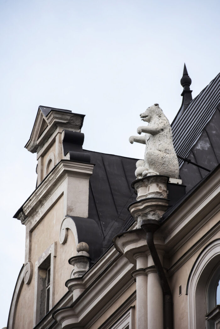 A fancy building with a turret and a balcony also has statues of bears perched on the edge of the roof.