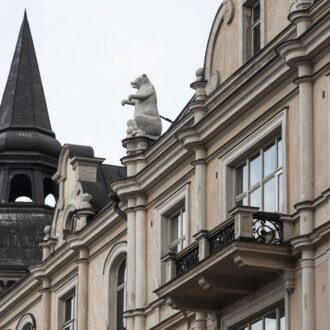 A fancy building with a turret and a balcony also has a statue of a bear perched on the edge of the roof.