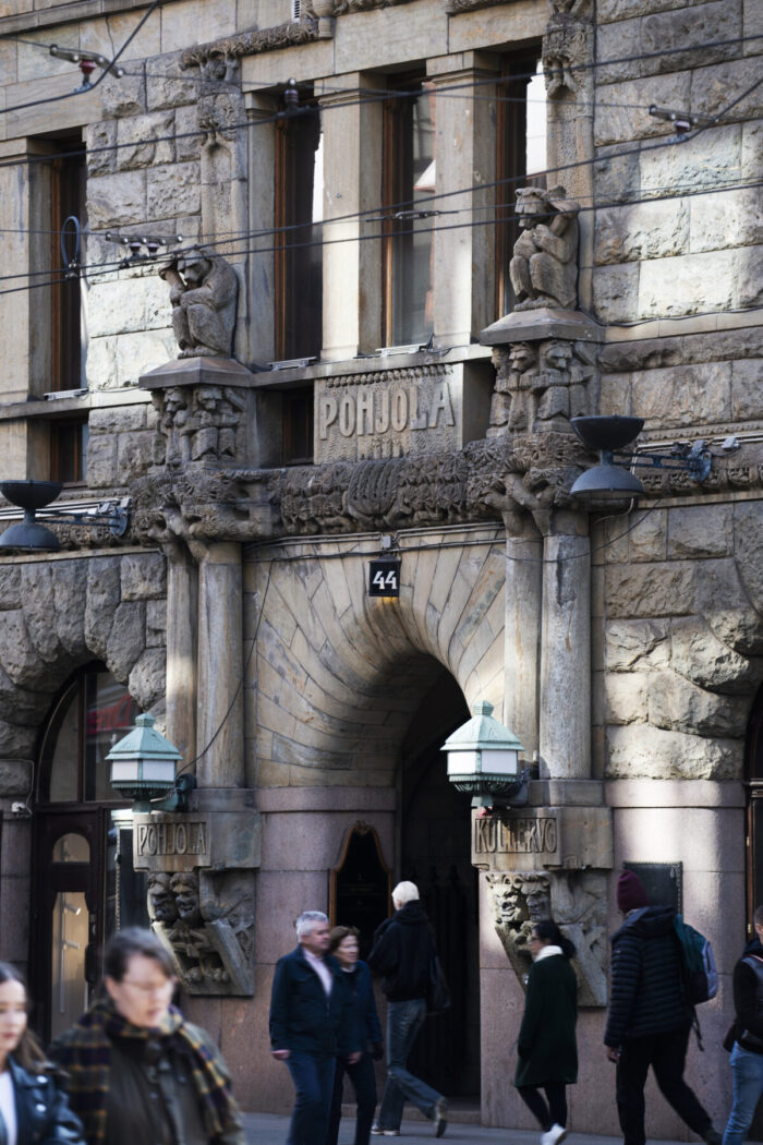 A grey stone building in downtown Helsinki is decorated with faces and statues of animals and mythical creatures.