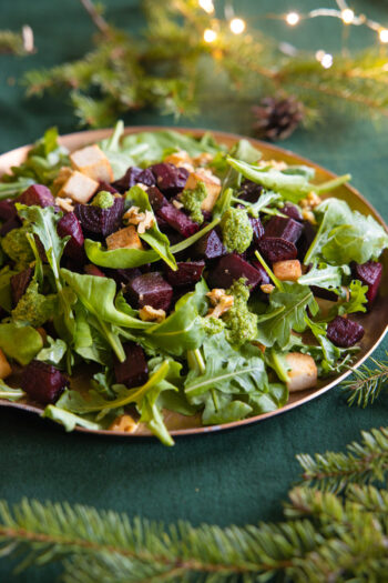 A dish holds a salad of chopped beets, chopped tofu and small green leaves.